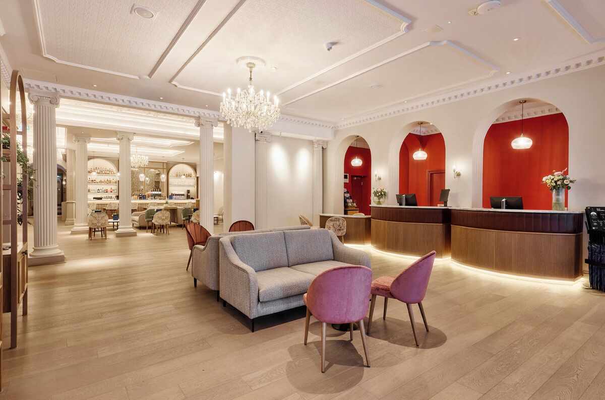 A hotel lobby with a reception desk, seating area, and a chandelier.
