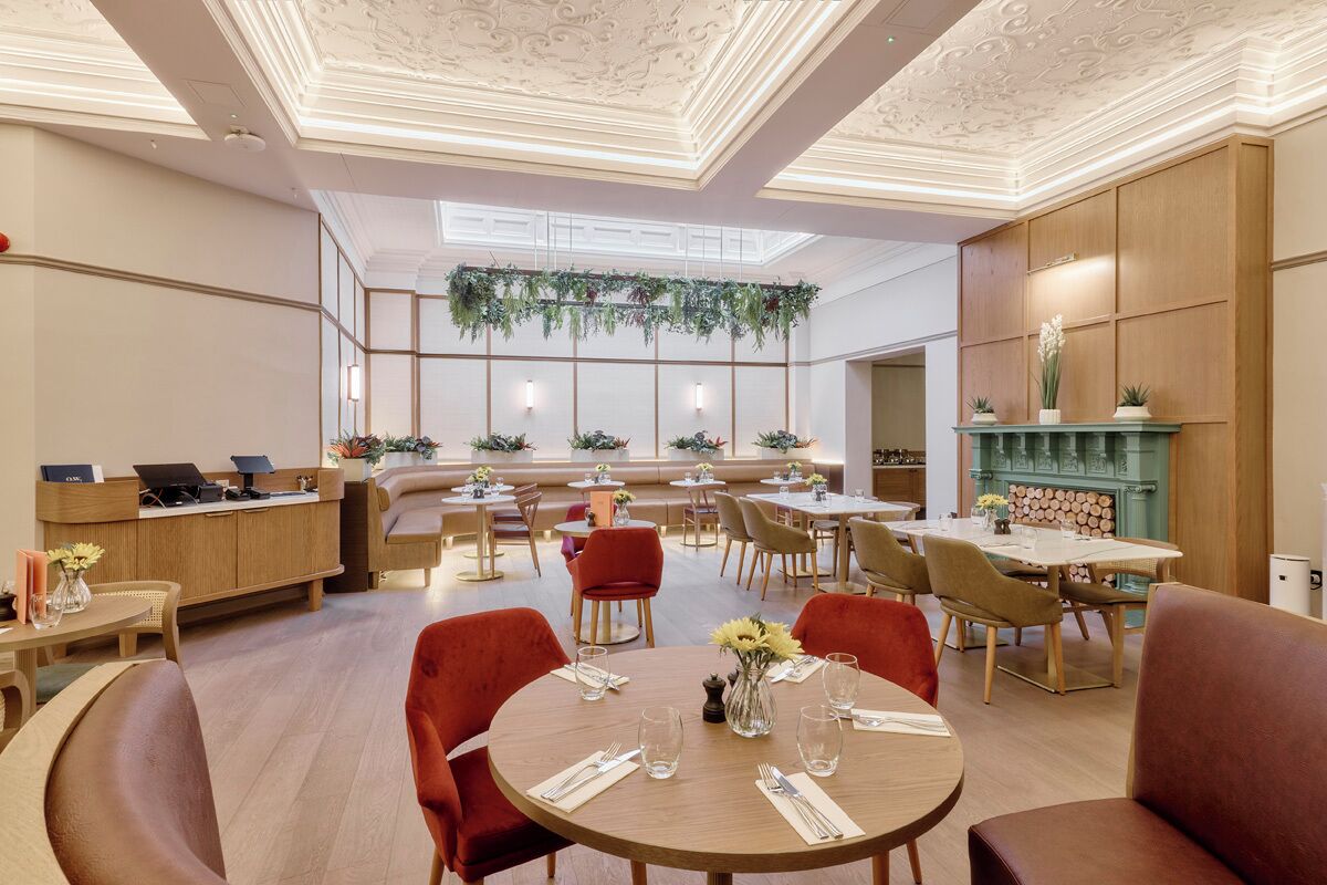 Un comedor de hotel con mesas redondas, sillas rojas y un mostrador de recepción.