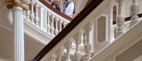 A grand staircase with ornate balustrades and columns, leading to an upper floor.