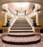 A grand staircase with a patterned carpet, leading to a high ceiling with a chandelier.