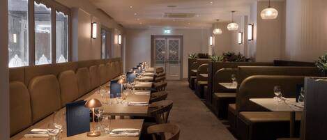 A restaurant with long tables, booths, and pendant lighting.