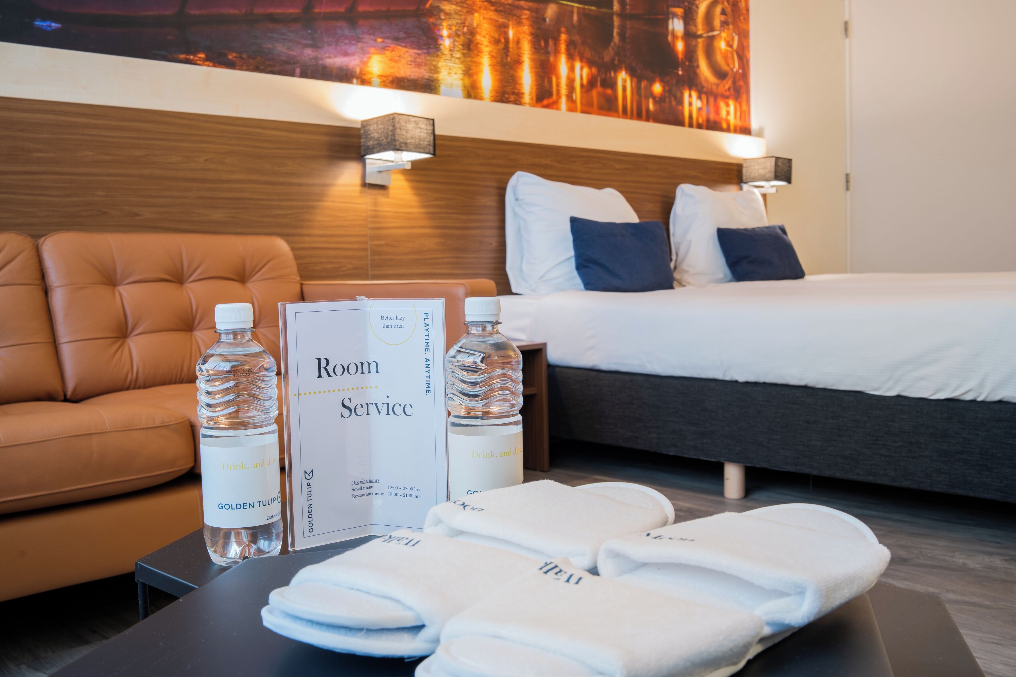 Habitación de hotel con cama, sofá y mesa, con comodidades como botellas de agua y toallas.