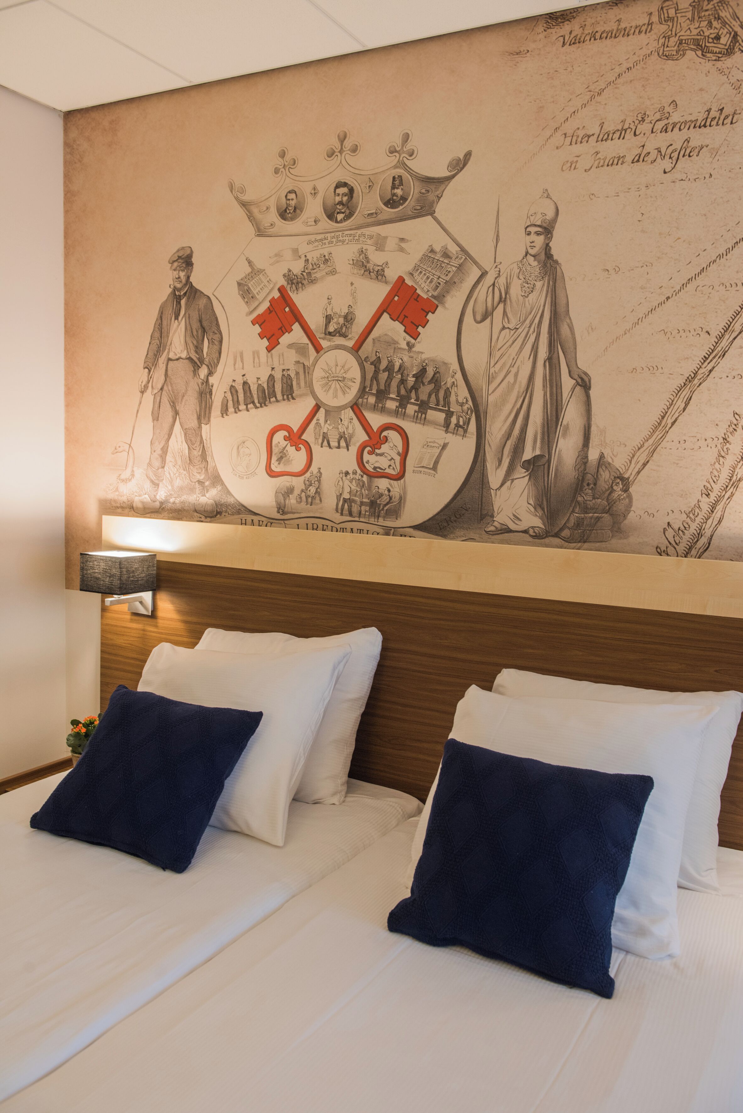 A hotel room with a large wall mural depicting historical figures and scenes, a wooden headboard, and two beds with white and navy blue bedding.