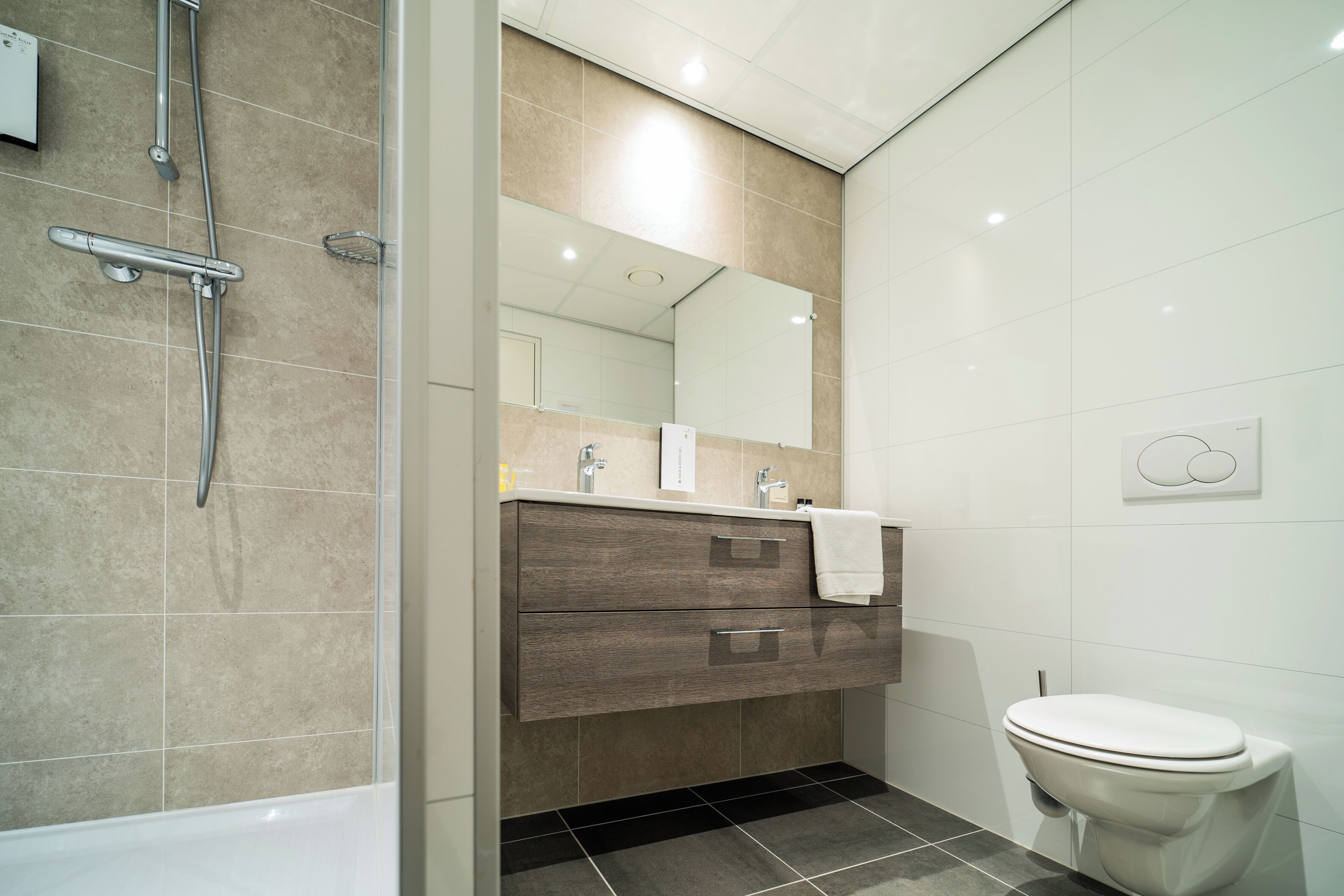 Een moderne badkamer met een bad, een douche, een wastafel met spiegel en een toilet.