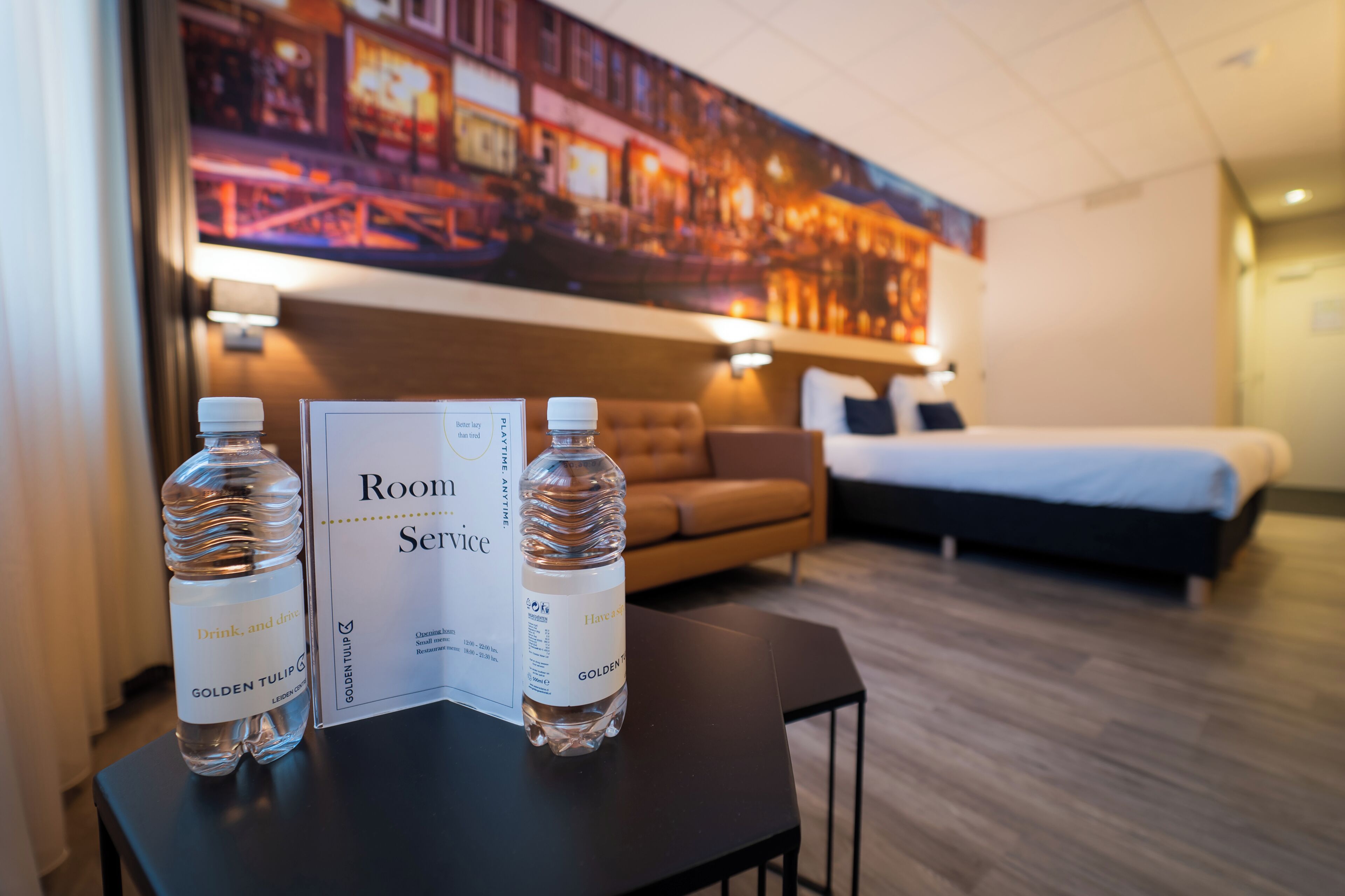 Ein Hotelzimmer mit Bett, Sofa und Tisch mit zwei Wasserflaschen sowie einer Speisekarte für den Zimmerservice.