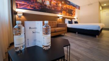 Ein Hotelzimmer mit Bett, Sofa und Tisch mit zwei Wasserflaschen sowie einer Speisekarte für den Zimmerservice.