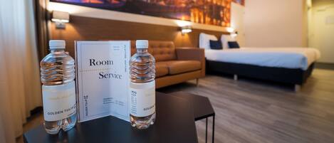 A hotel room with a bed, a sofa, and a table with two water bottles and a room service menu.