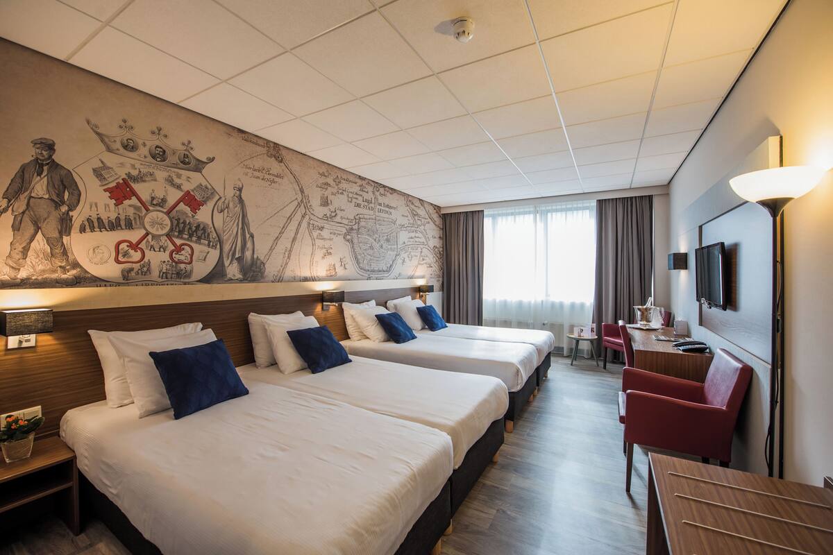 A hotel room with four beds, a dining area, a TV, and a mural on the wall.