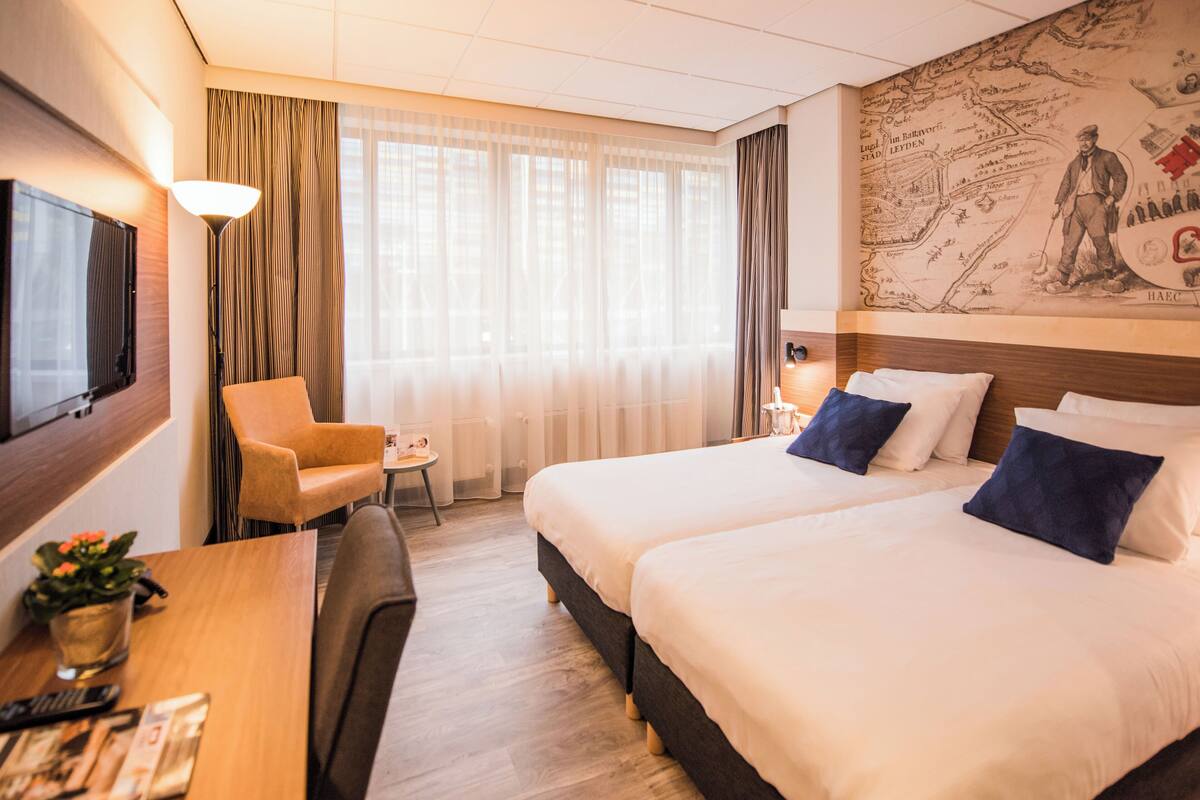 A hotel room with two beds, a desk with a chair, a TV, and a map on the wall.