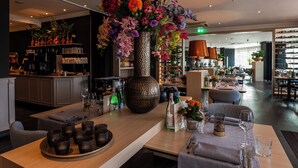 Un restaurante con un gran centro de mesa floral, una zona de bar y diferentes disposiciones de mesas.