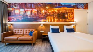 A hotel room with a bed, a sofa, a nightstand, and a wall mural of a cityscape.