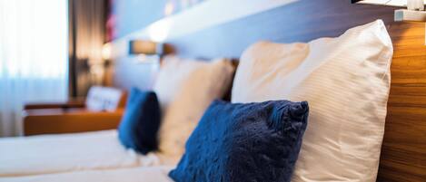 Una habitación de hotel con cama, almohadas, mesita de noche y lámpara.
