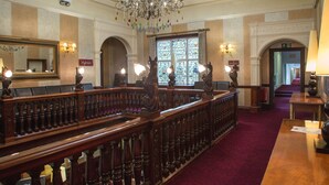 A grand hall with a wooden railing, chandeliers, and a red carpet.