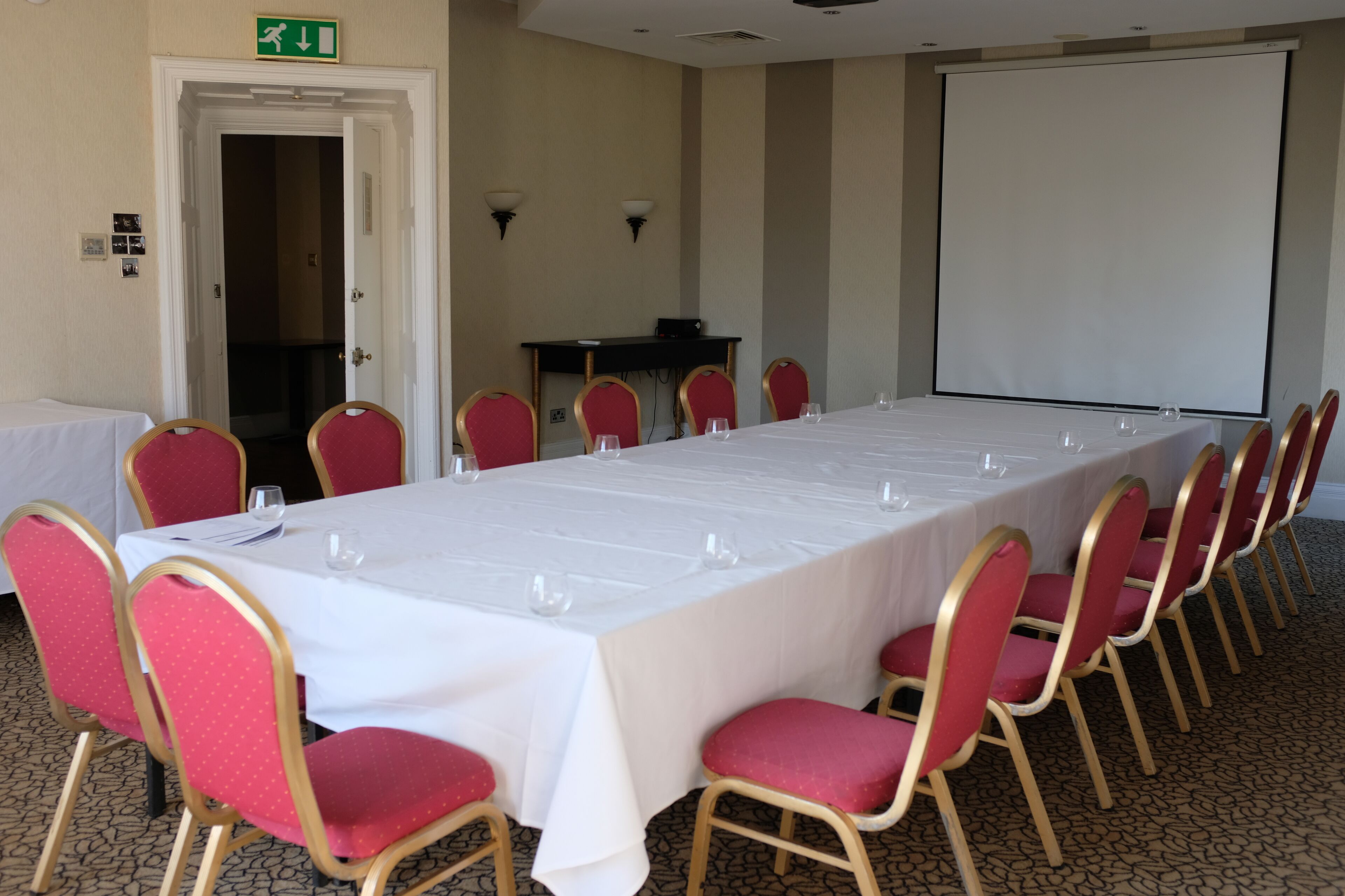 A conference room with a long table, red chairs, a projector screen, and a whiteboard.