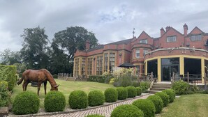 A large brick building with a covered outdoor area, a horse grazing in the garden, and well-maintained hedges. - The Mount Country Manor Hotel & Golf (Wolverhampton)