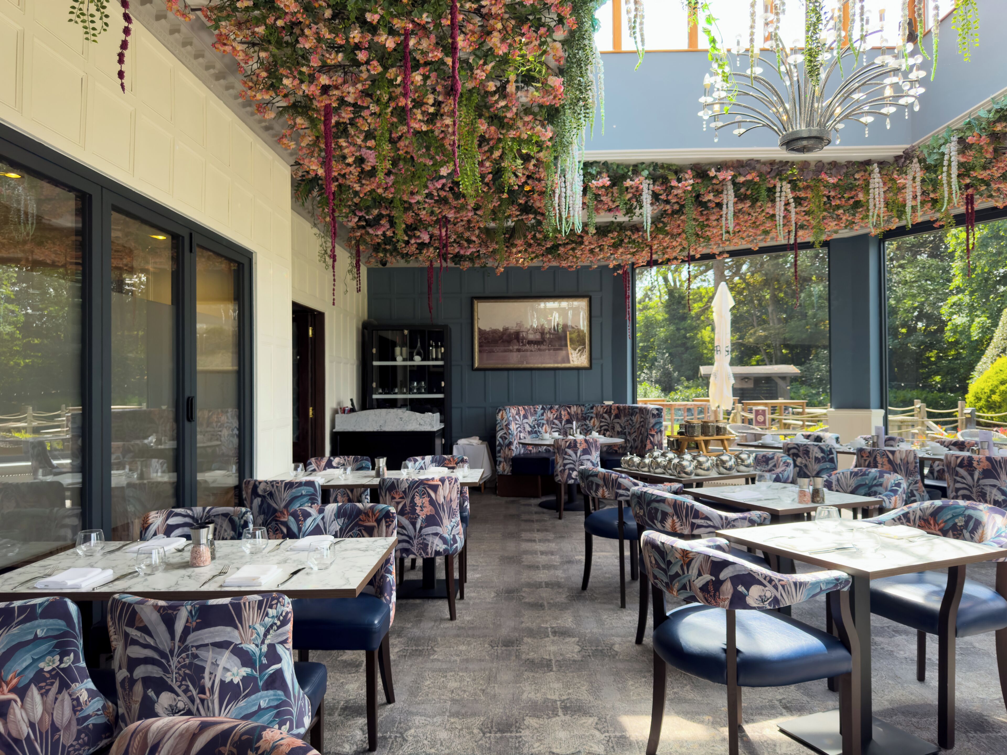 A restaurant with outdoor seating, floral decorations, and a view of the garden.