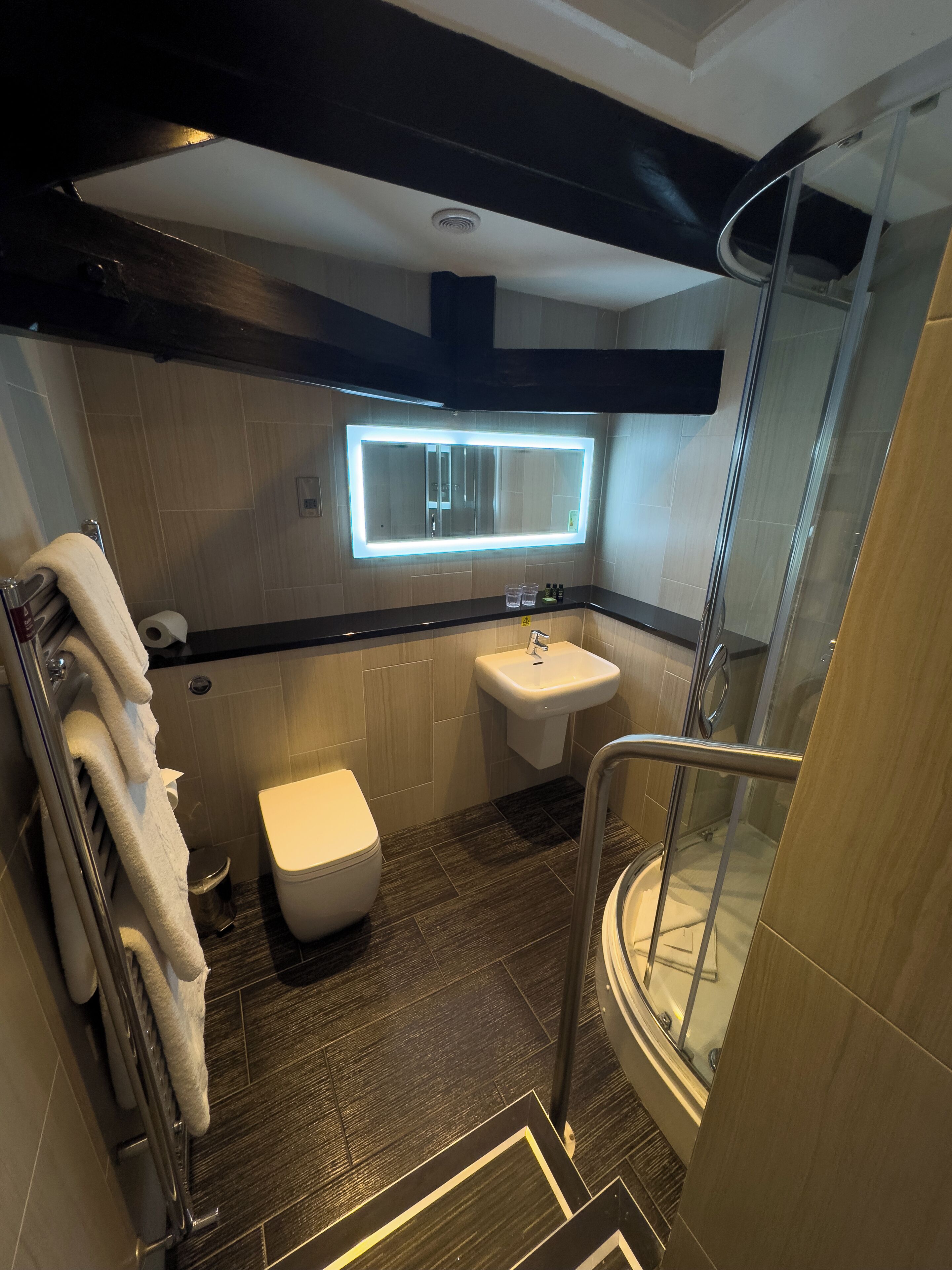 A modern bathroom with a glass shower, a white toilet, a sink, and a mirror with built-in lighting.