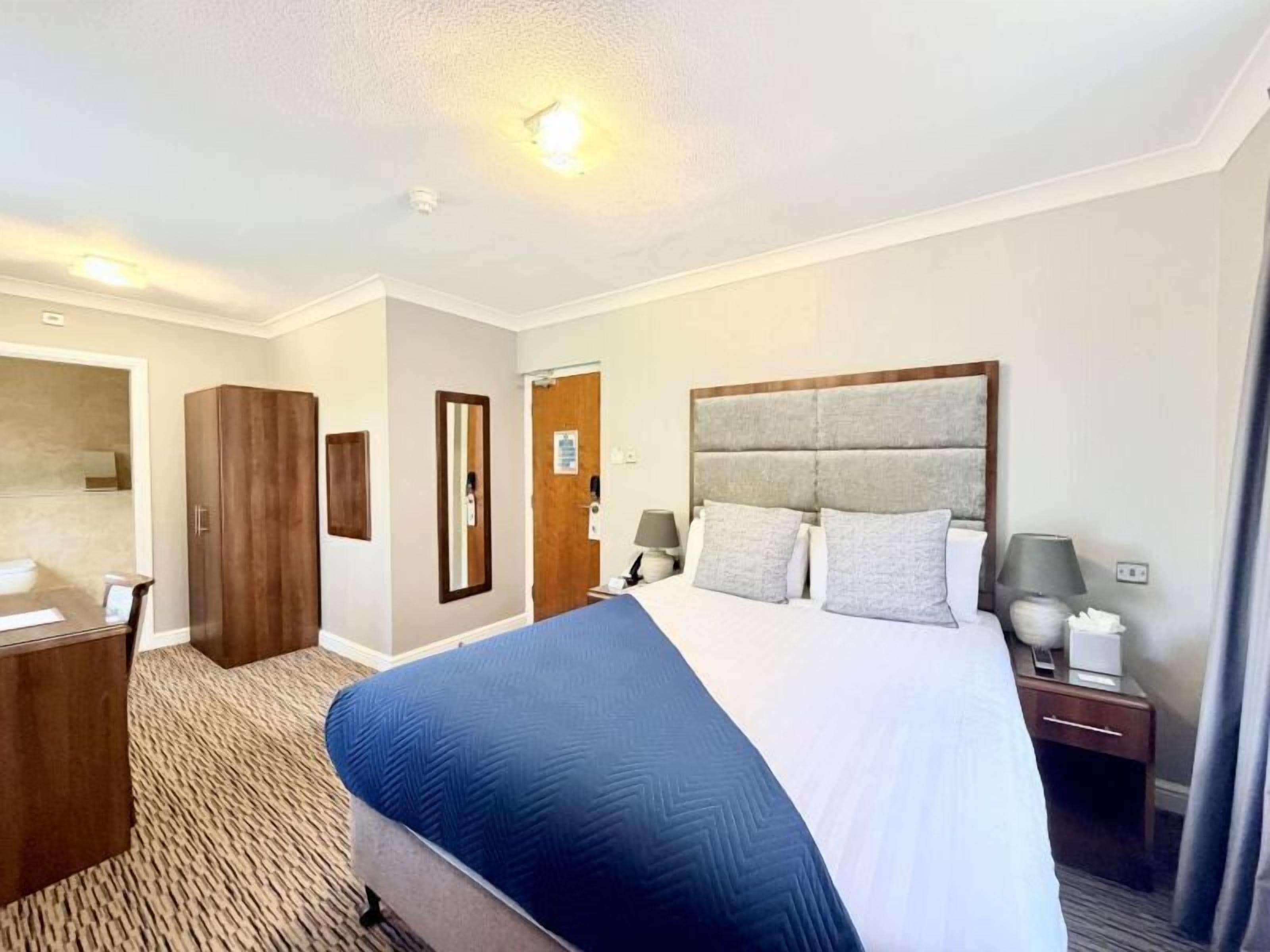 Habitación de hotel con una cama grande, un armario de madera, un escritorio y un espejo.
