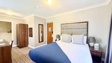 Habitación de hotel con una cama grande, un armario de madera, un escritorio y un espejo.