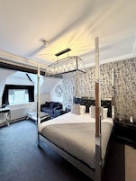 Quarto de hotel moderno com uma cama de dossel, uma escrivaninha e um espaço de estar aconchegante.