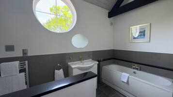 A bathroom with a round window, a sink, a mirror, a bathtub, and a towel rack.
