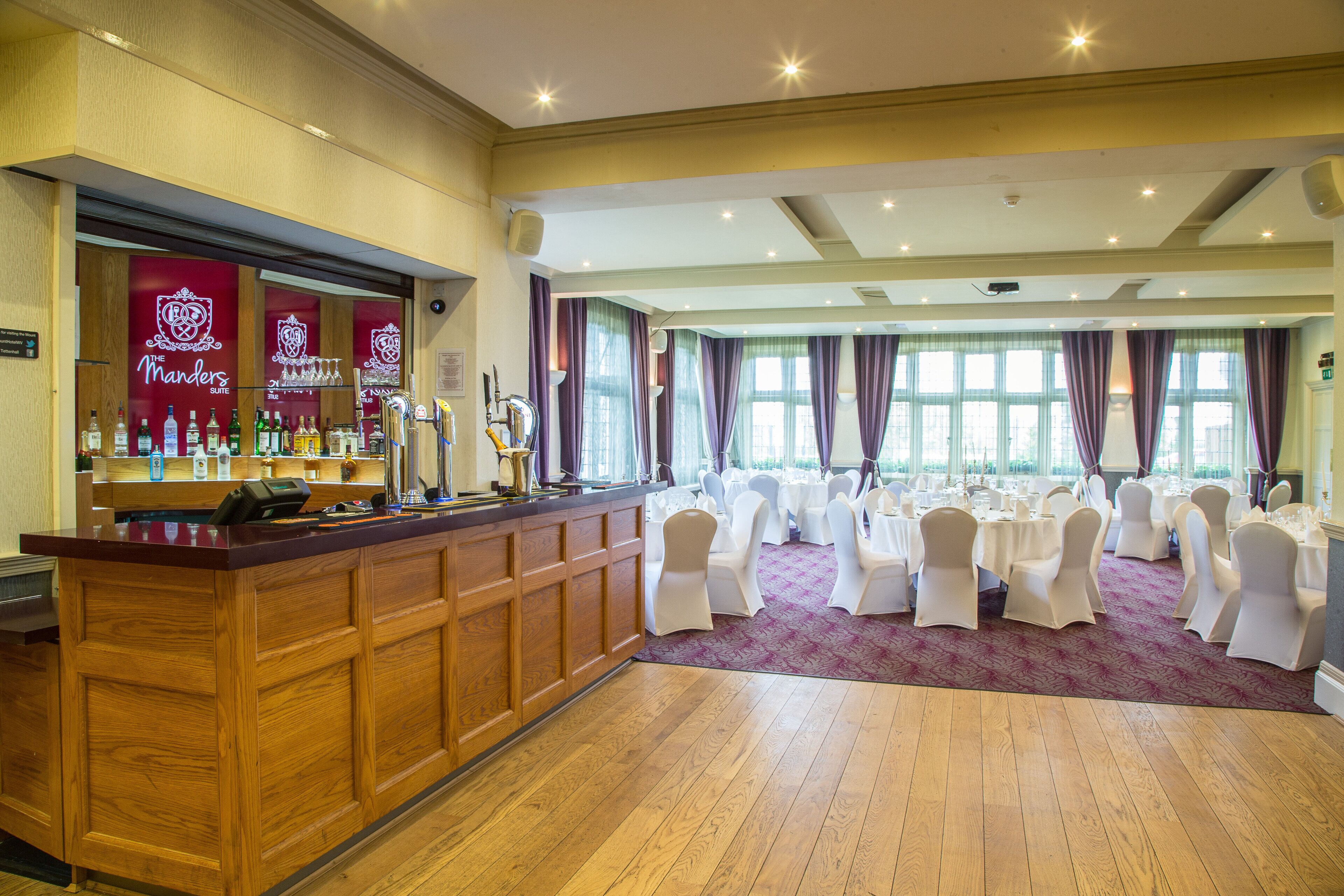A hotel lobby with a bar area, round tables, and white chairs.