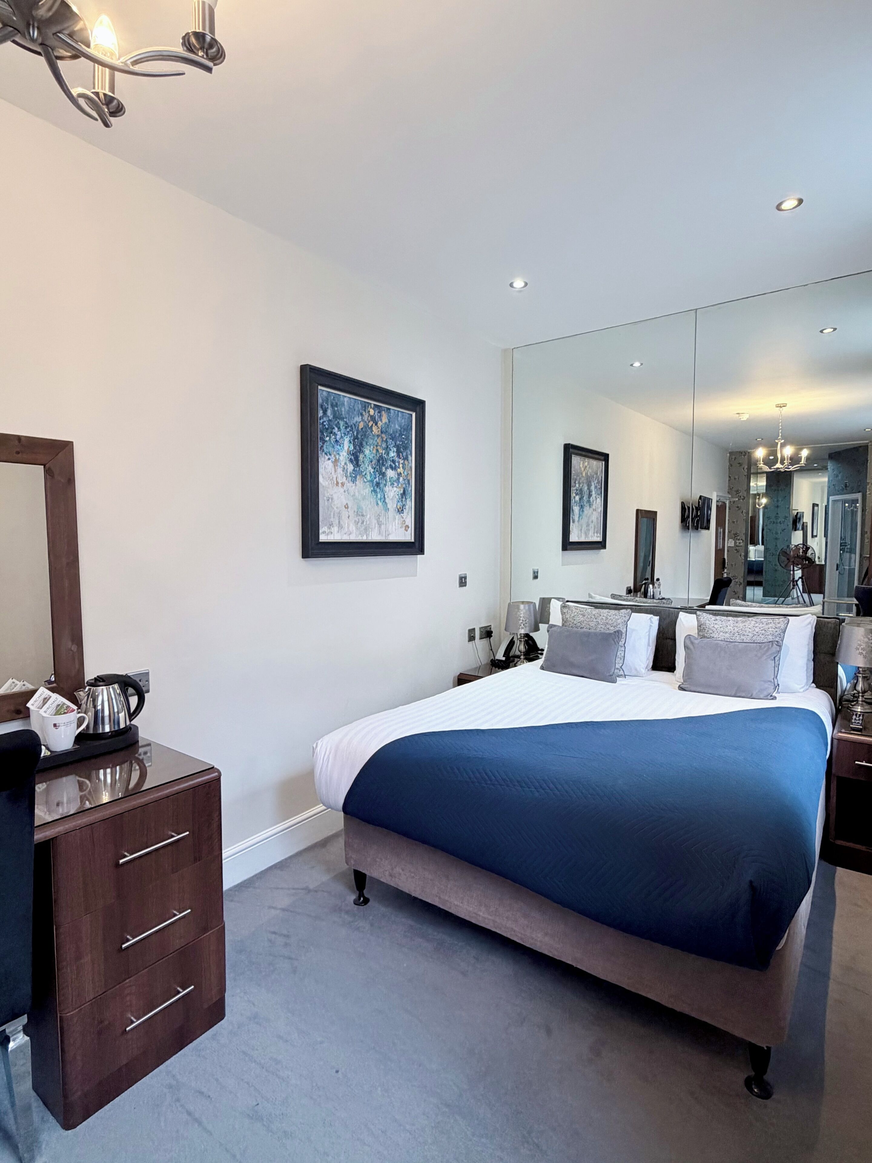 A modern hotel room with a large bed, a dresser, a mirror, and a painting on the wall.