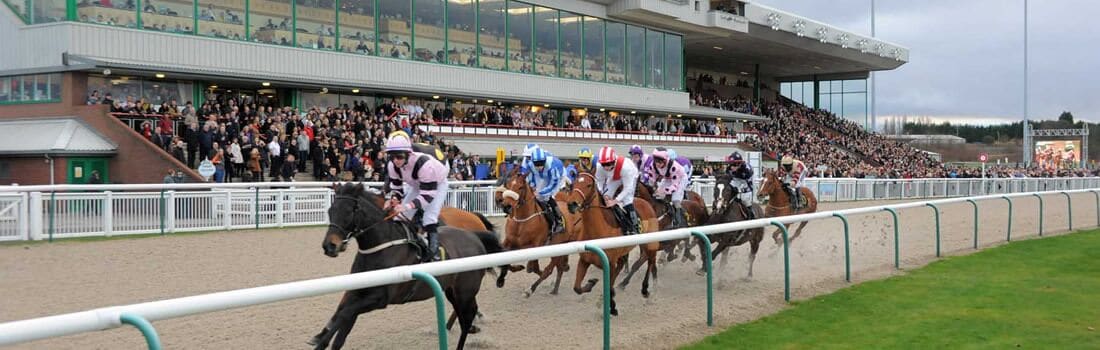 A horse race with jockeys on horses, a crowd of spectators, and a grandstand.