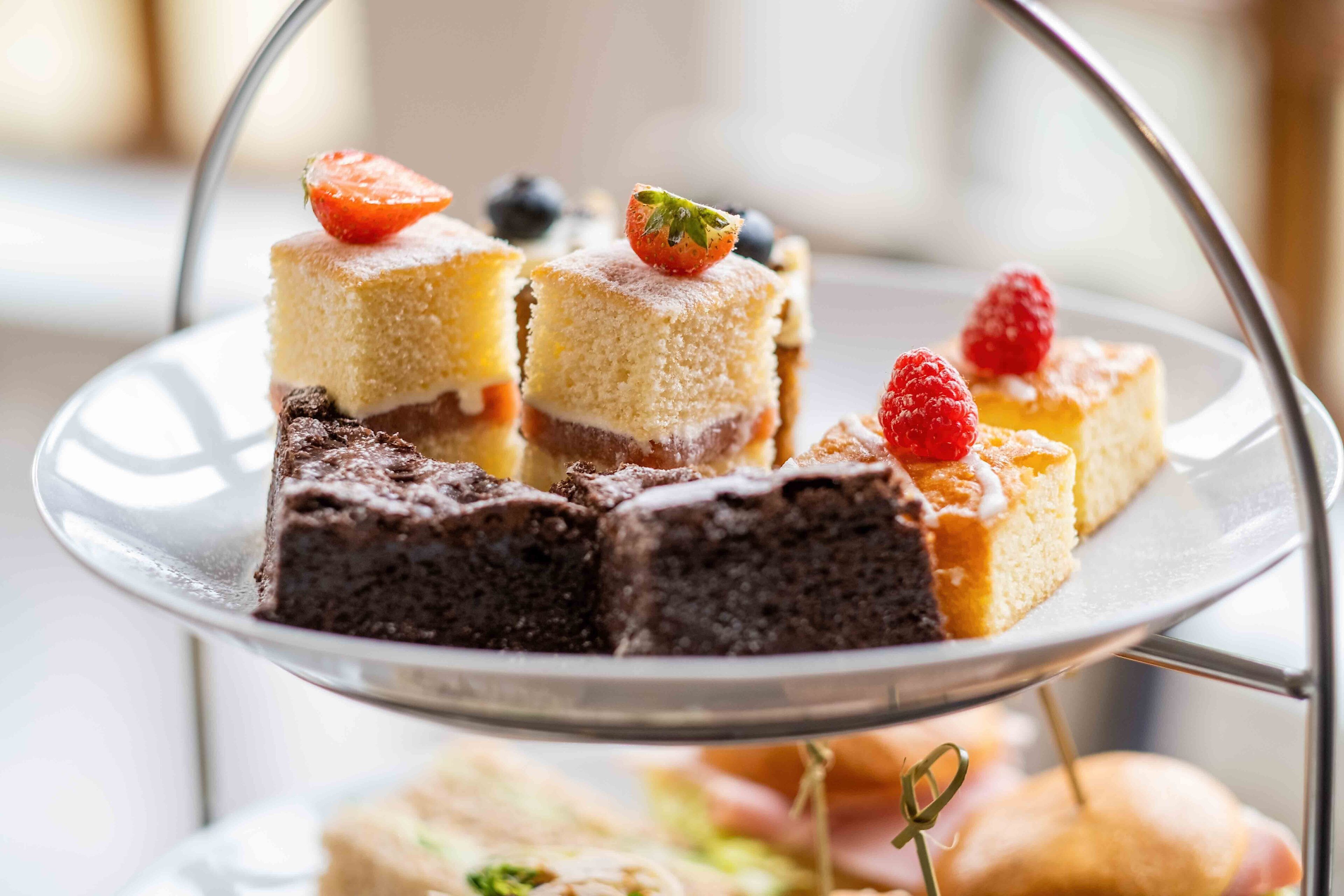 Una bandeja escalonada con diversos postres, incluyendo pasteles y brownies, adornada con fresas y arándanos.