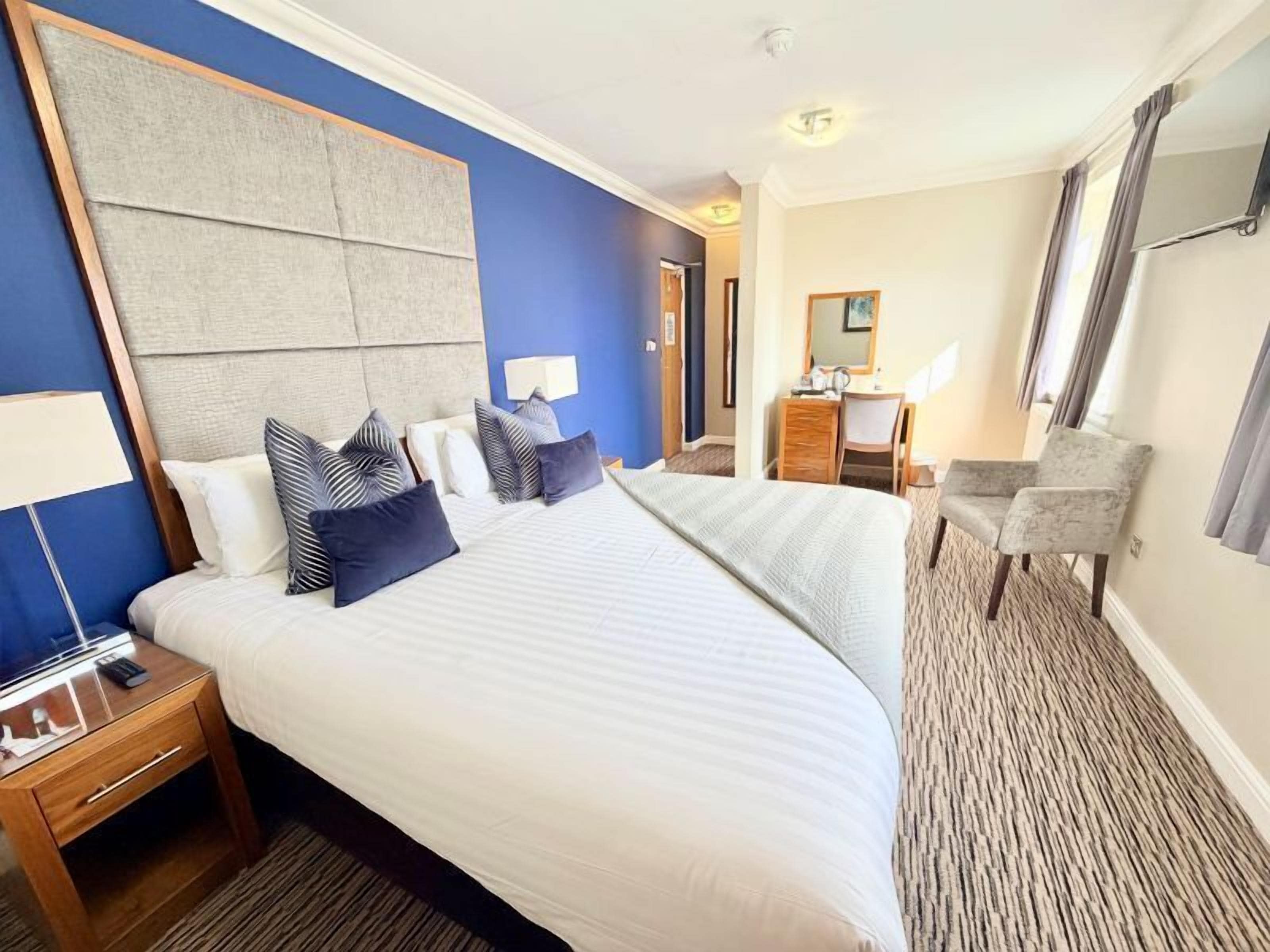 A hotel room with a large bed, a desk, a chair, and a mirror.