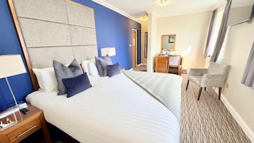 A hotel room with a large bed, a desk, a chair, and a mirror.