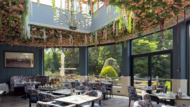 A restaurant with a high ceiling, hanging floral decorations, and large windows offering a view of the outdoors. - The Mount Country Manor Hotel & Golf (Wolverhampton)