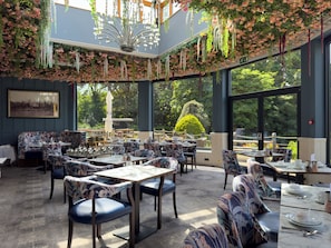 Un restaurant avec un plafond haut, des décorations florales suspendues et de grandes fenêtres donnant sur l’extérieur.
