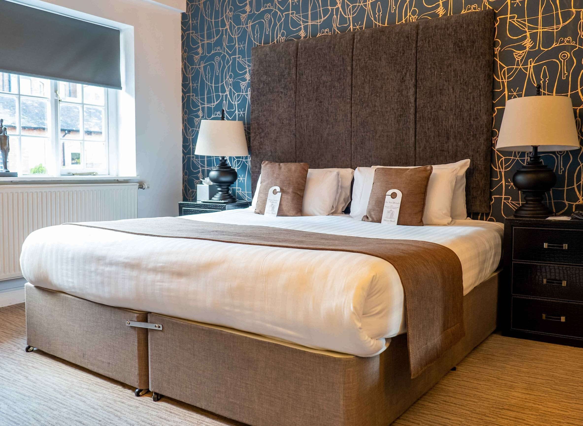 Hotellihuone, jossa on suuri sänky, yöpöytä valaisimineen ja ikkuna, josta on näkymä.