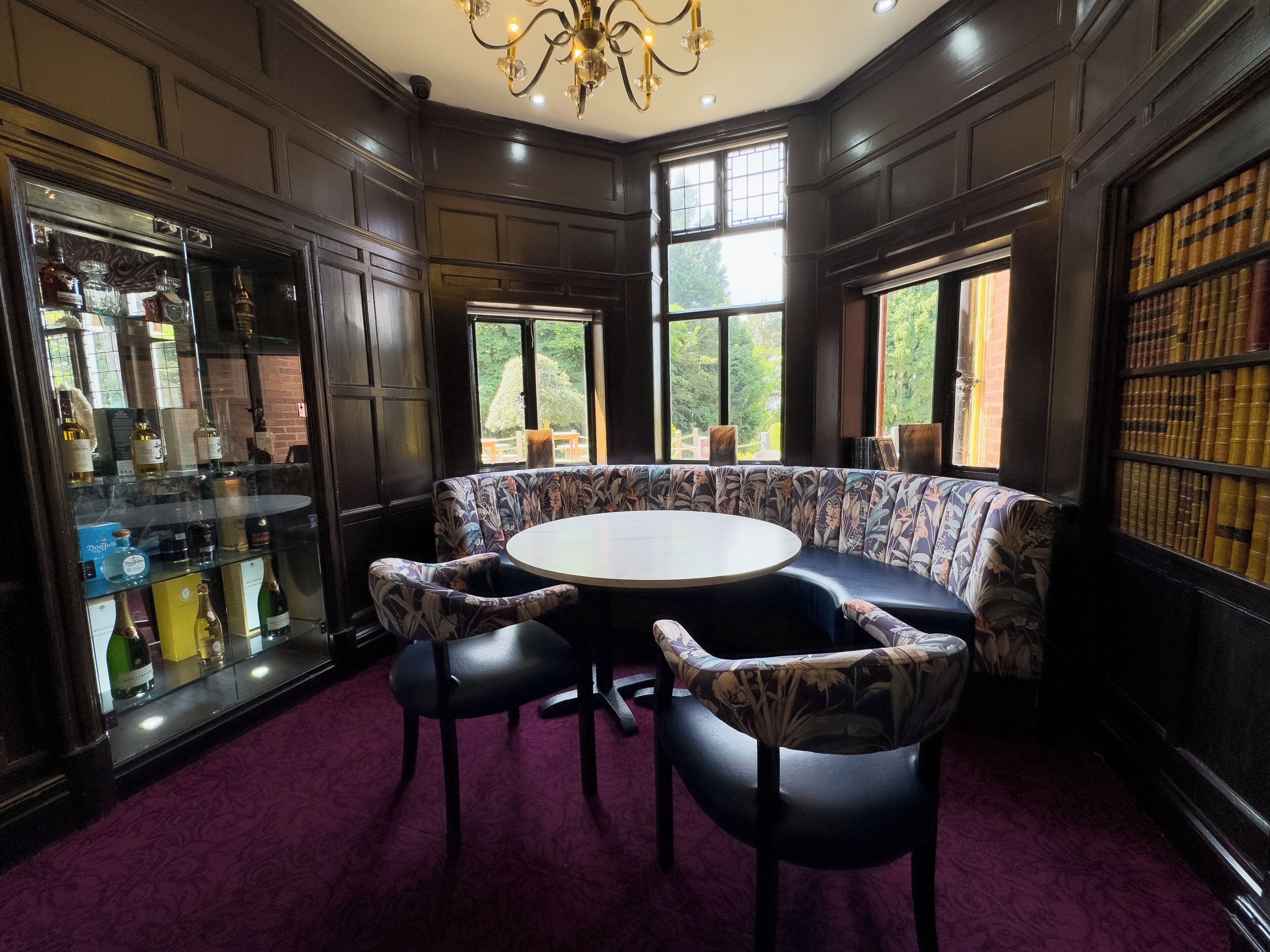 A room with a round table, two chairs, a bookshelf, and a glass display case.