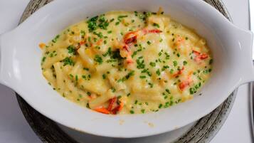 Un plato blanco ovalado con pasta, queso derretido y cebollines, sobre un posavasos tejido.