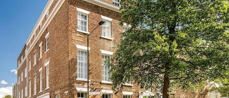 A multi-story brick building with white window frames, a sign indicating 'Park Street,' and a tree in the foreground.