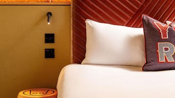Habitación de hotel con cama, cabecera, mesita de noche y panel de control en la pared.