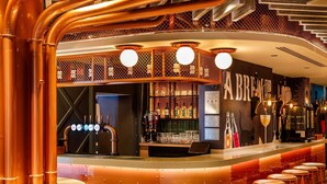 Um bar com tubos de cobre, banquetas e um balcão com um laptop.