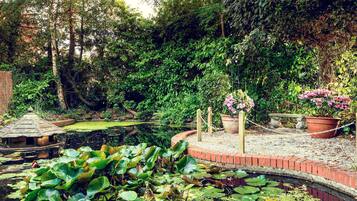 A garden with a pond, potted plants, and a brick pathway.