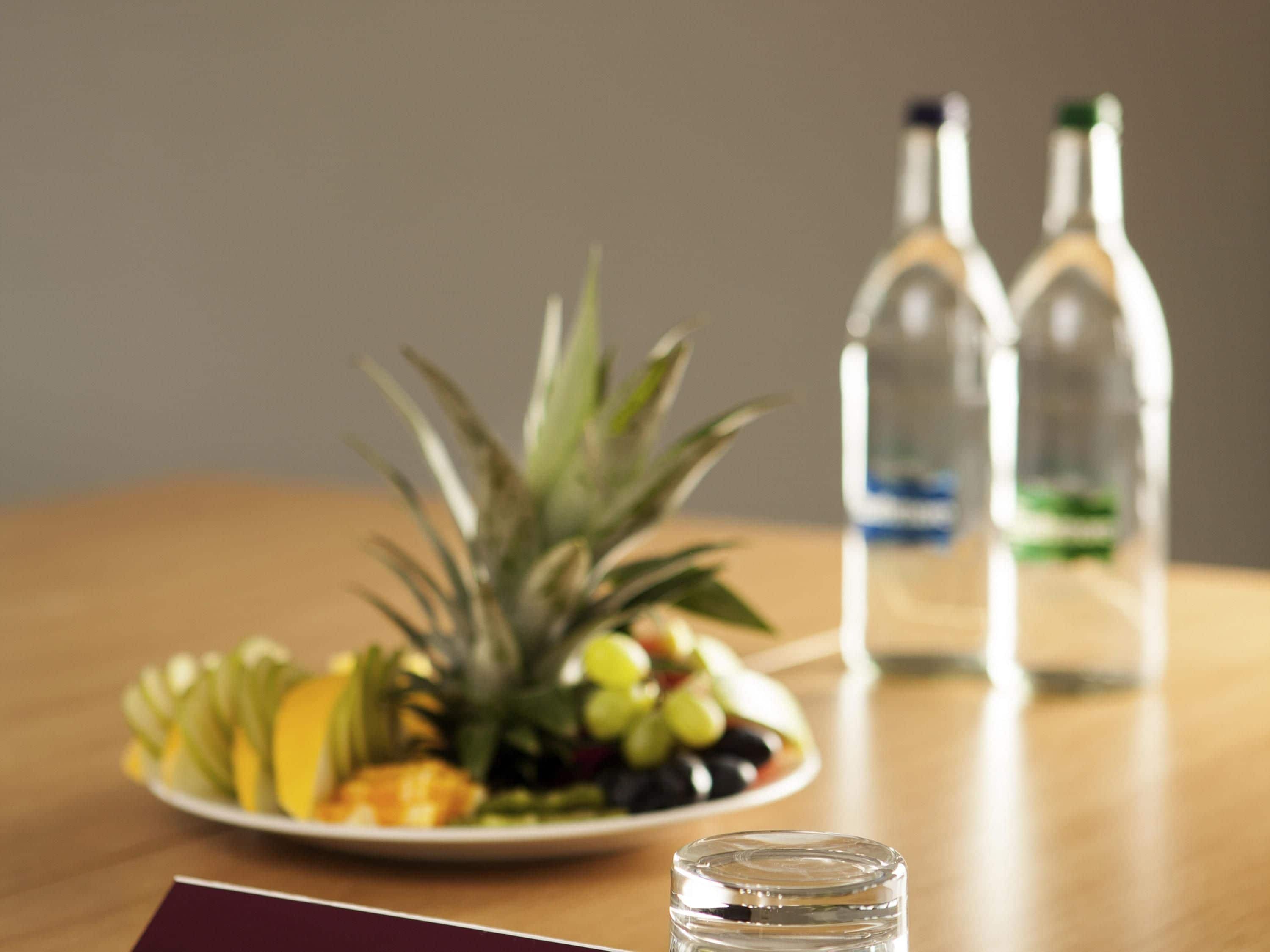 A wooden table with a plate of fruit, two bottles of clear liquid, and a small glass.
