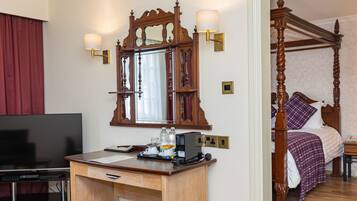 A hotel room with a wooden desk, a television, a four-poster bed, and a large mirror with wall sconces.