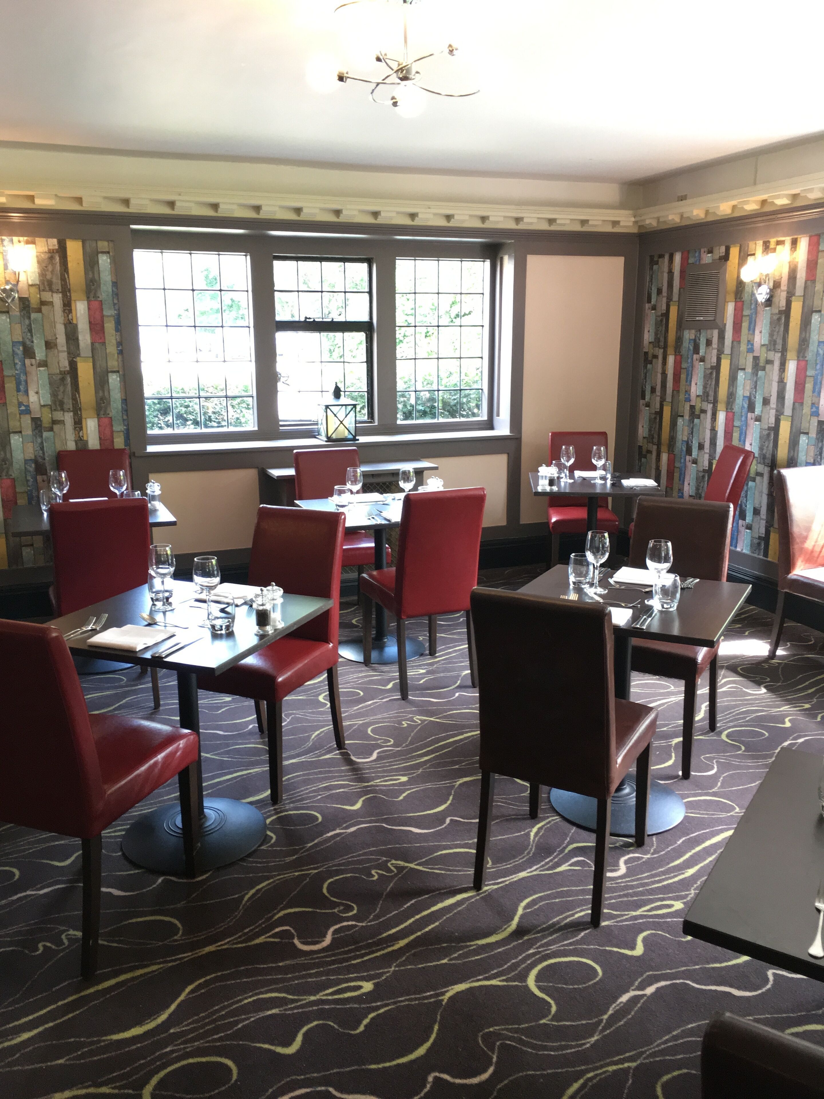 A restaurant with red chairs and tables, large windows with a view, and a patterned carpet.
