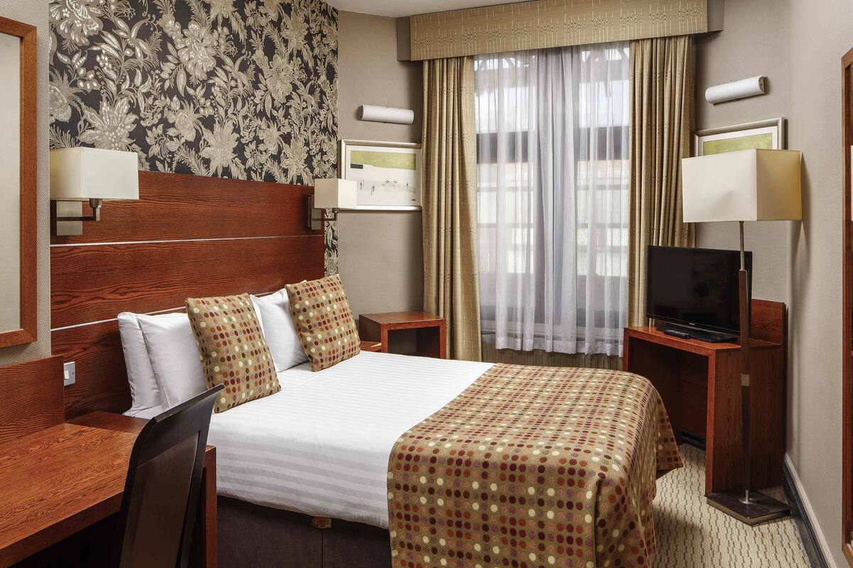 Une chambre d’hôtel avec un grand lit, un bureau, une télévision et une fenêtre avec des rideaux.