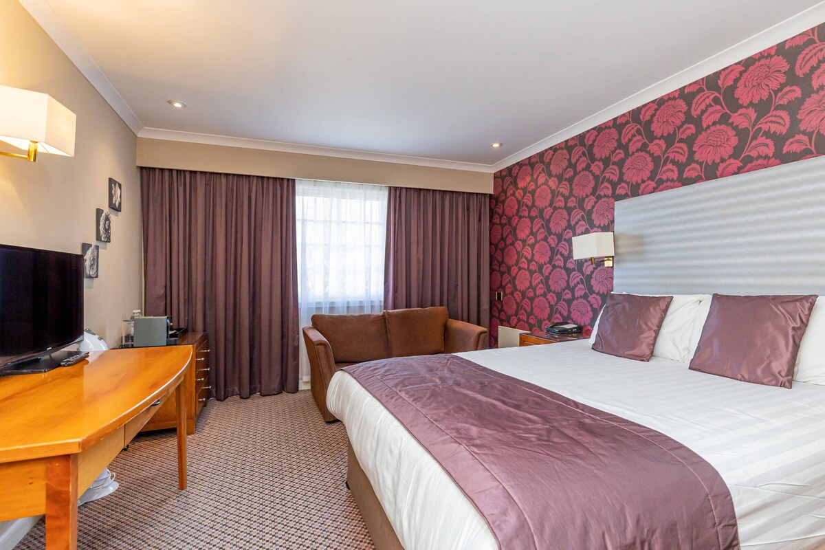 Een hotelkamer met een groot bed, een bureau met televisie, een stoel en een raam met gordijnen.