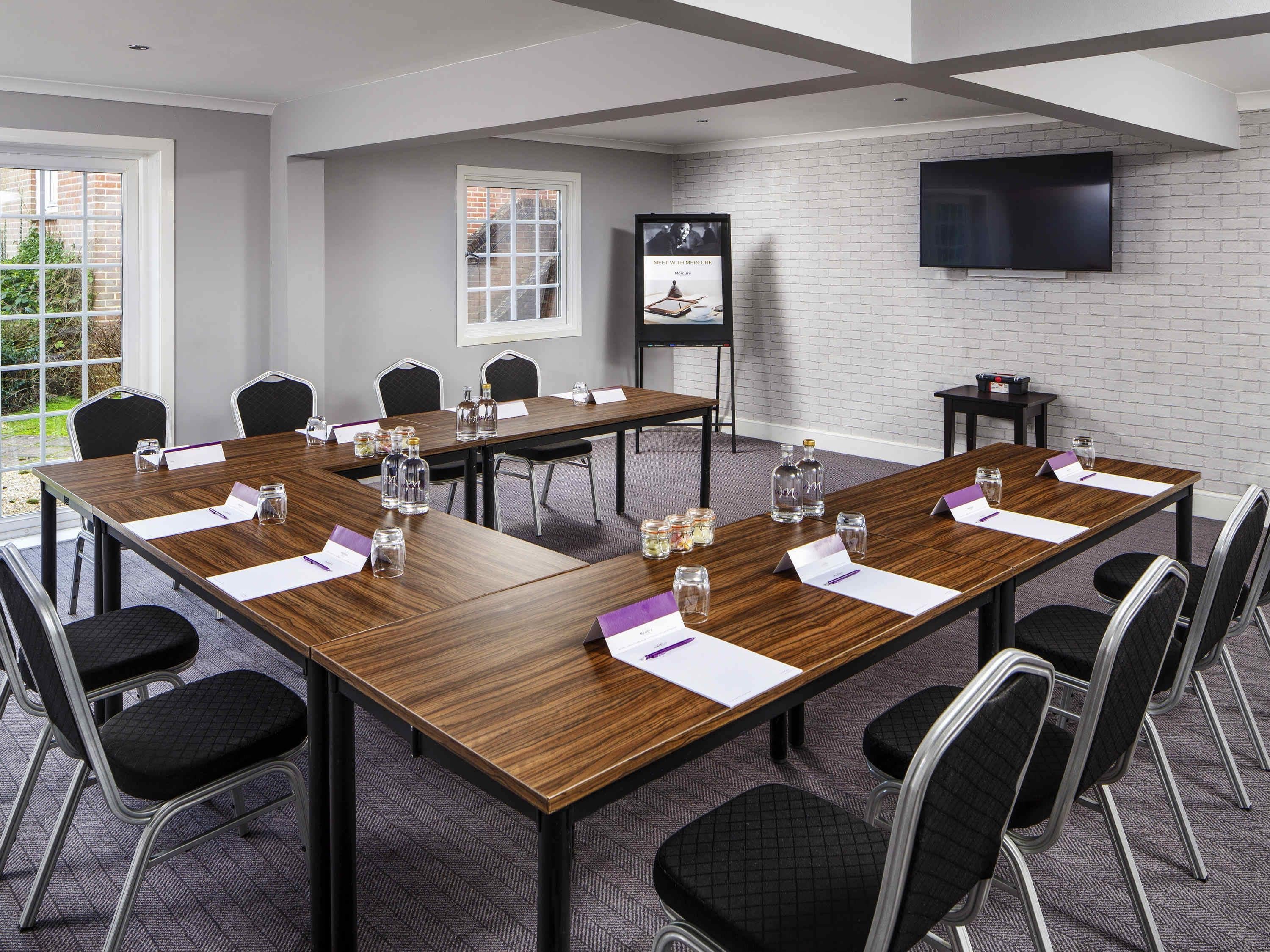 A conference room with a long table, chairs, a TV, and a poster on the wall.