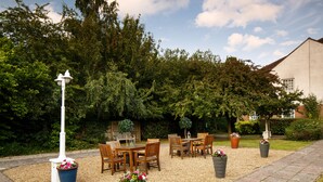 Un espace extérieur aménagé avec des tables et des chaises, entouré d’arbres et avec un bâtiment en arrière-plan.