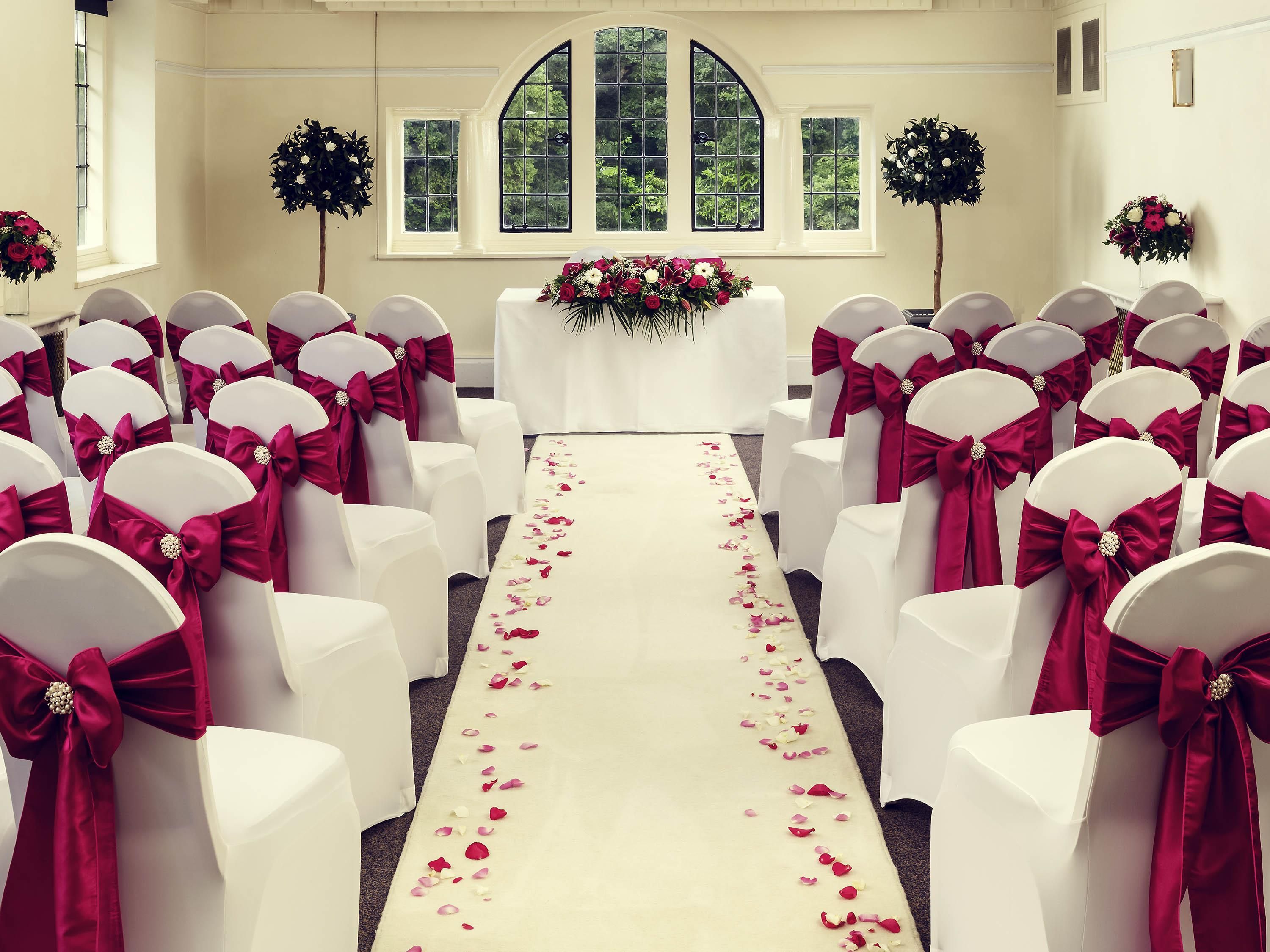 A church interior with pews arranged in rows, a white aisle with rose petals, and floral decorations.