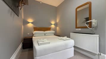 A neatly made bed with white linens, a wooden headboard, and a white radiator below.