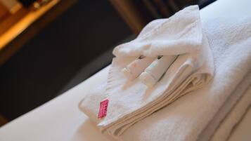 A neatly folded white towel with a pink tag and two small bottles on top, likely containing lotion or soap, placed on a white surface.